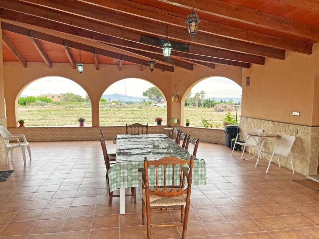 Terraza con mesa grande y sillas, vistas a un campo