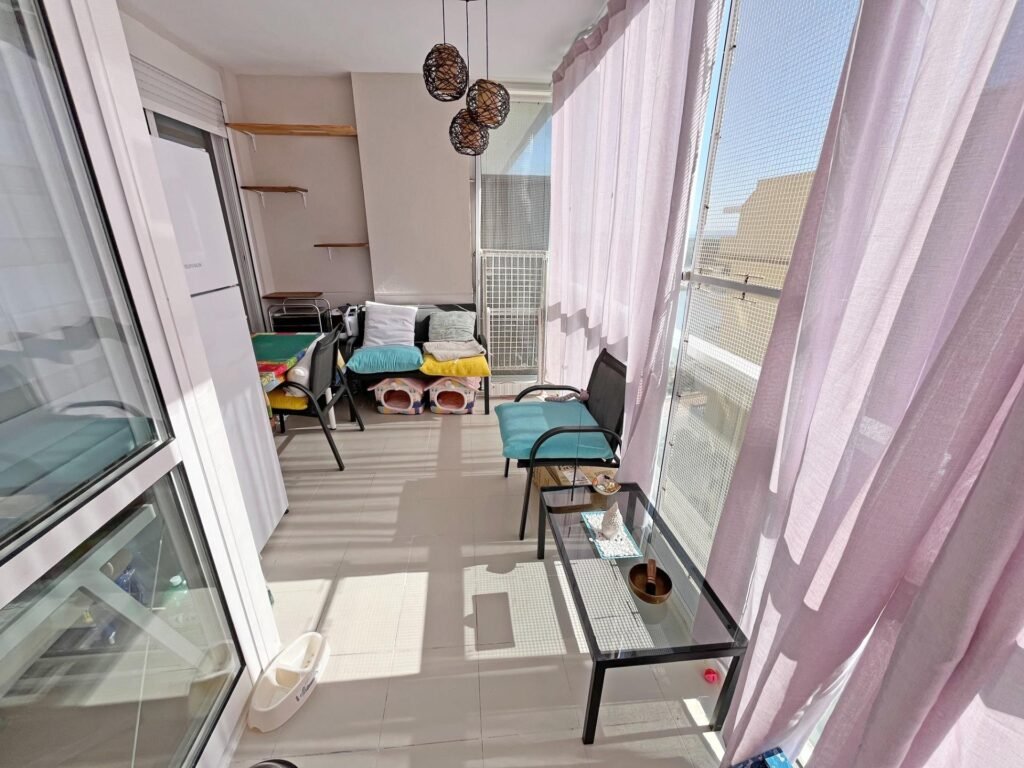 Balcón con sillones, mesa de vidrio y cortinas translúcidas