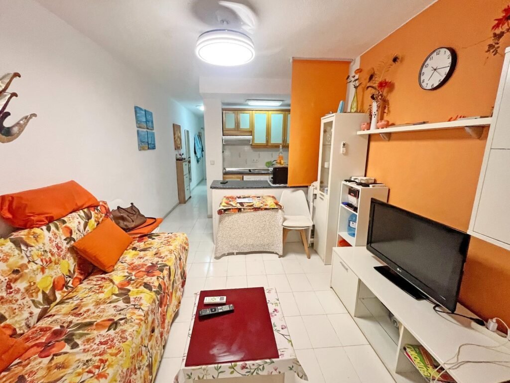 Sala acogedora con sofá floral y cocina al fondo
